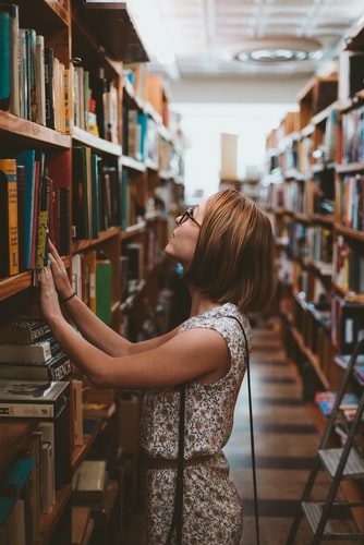 a woman looking at a book on a shelf