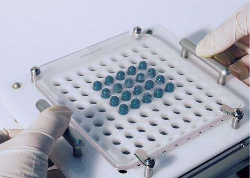 a close-up of a gloved hand holding a tray with blue pills