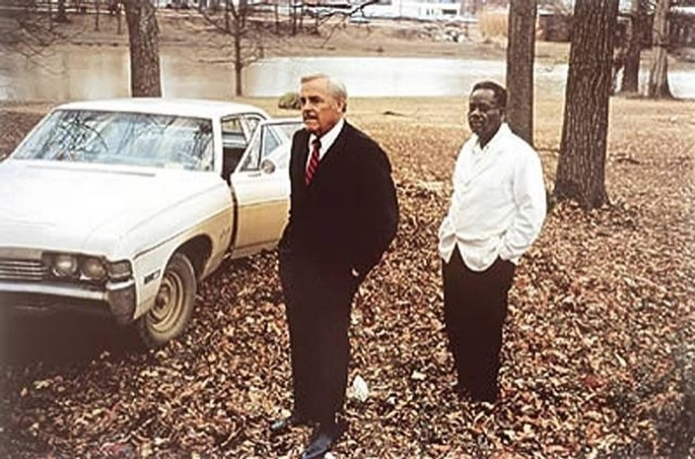 a couple of men standing in leaves next to a car