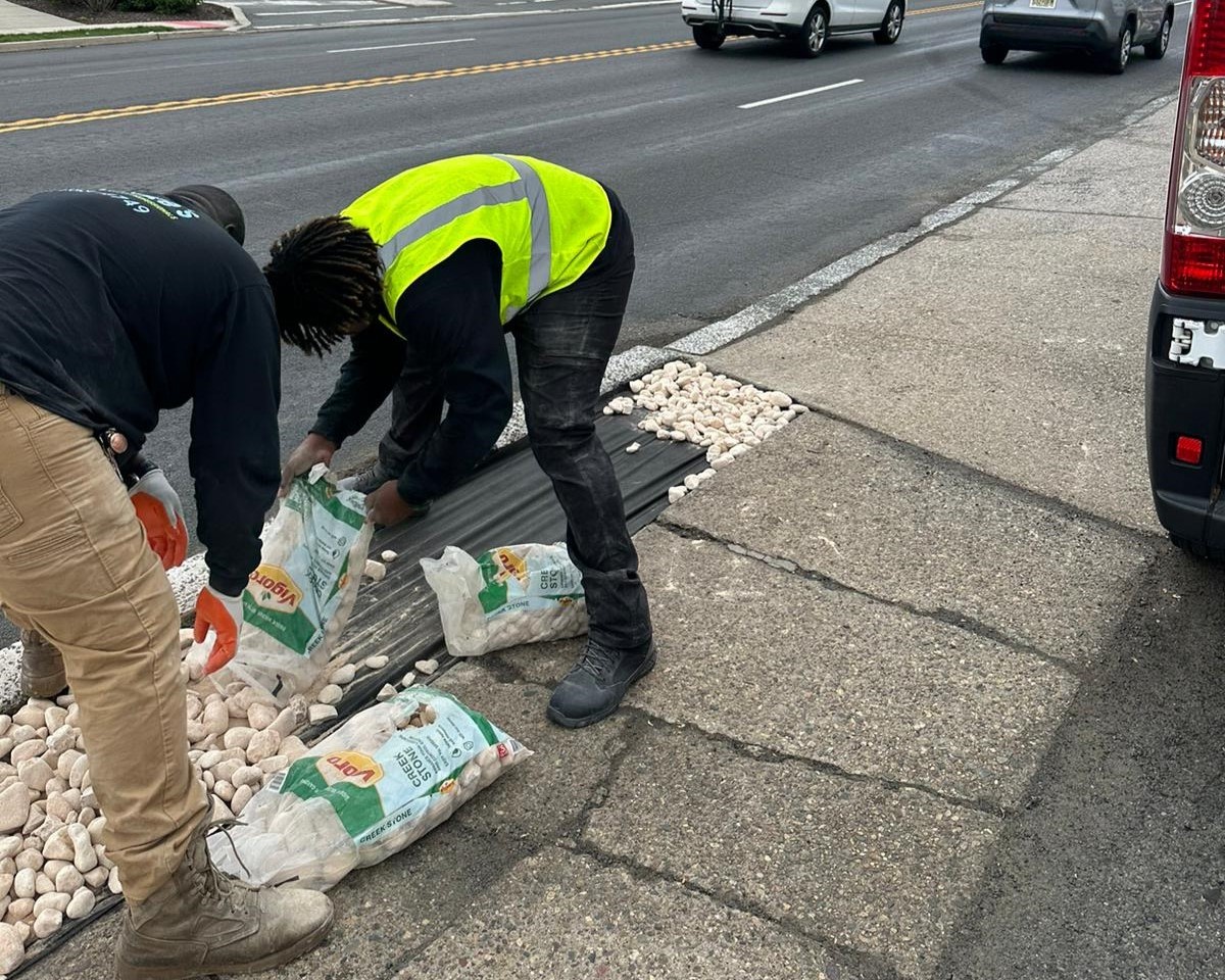 a group of men in reflective vests picking up rocks on a sidewalk