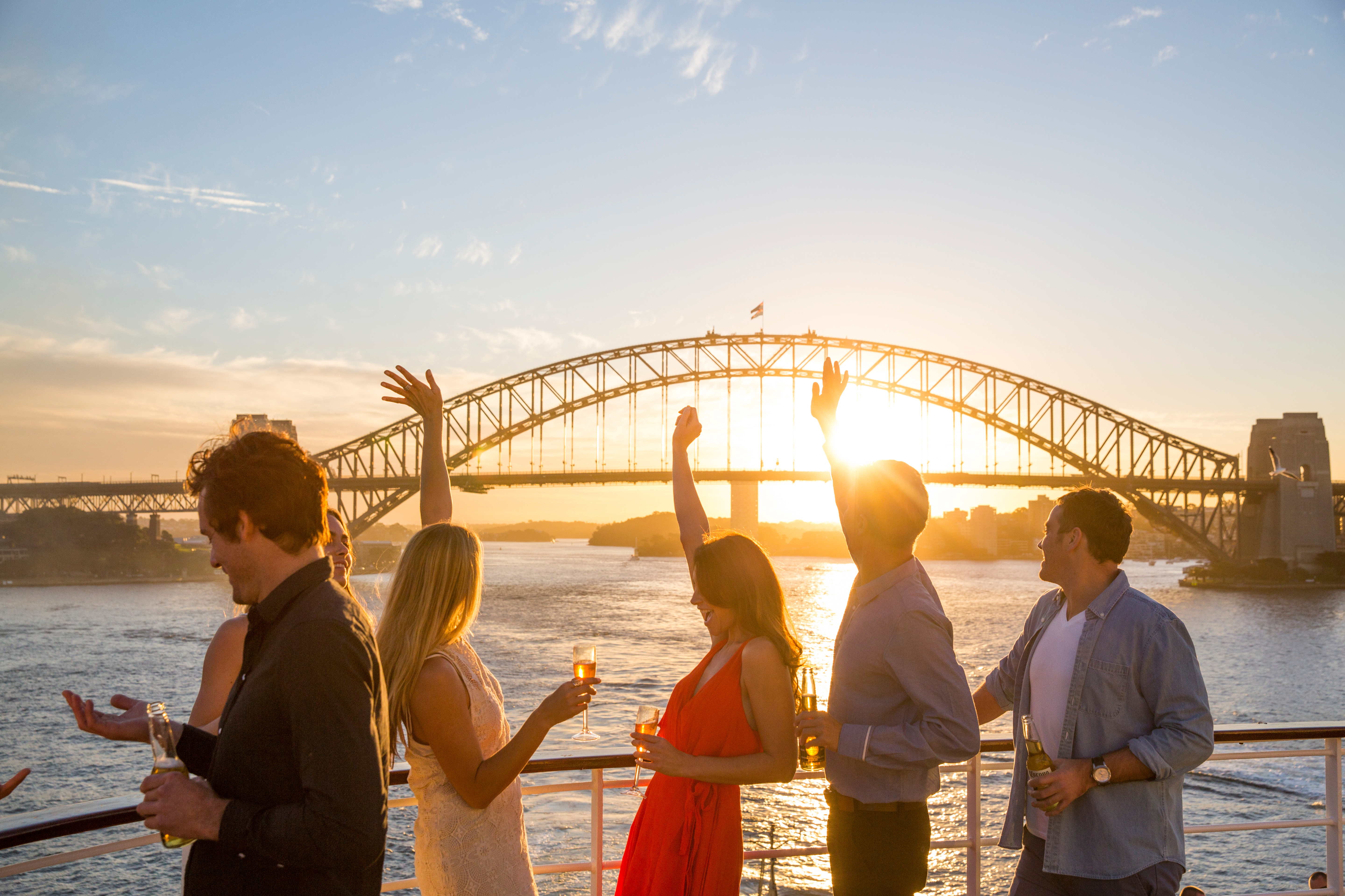 a group of people standing on a boat with drinks and a bridge in the background