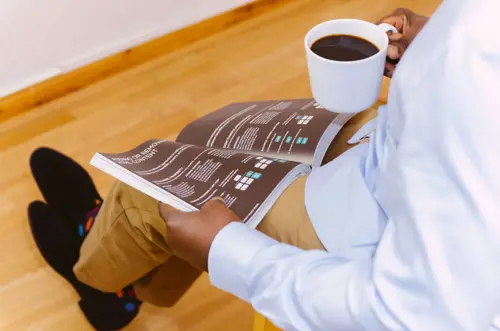 a person holding a cup of coffee and reading a magazine