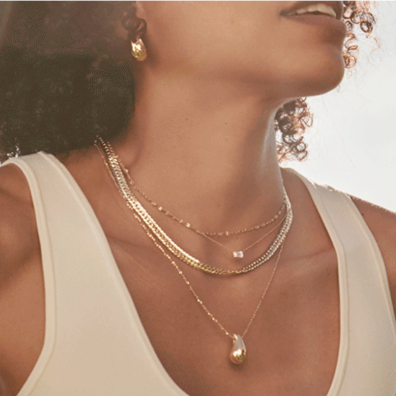 a woman wearing a white tank top and gold necklaces