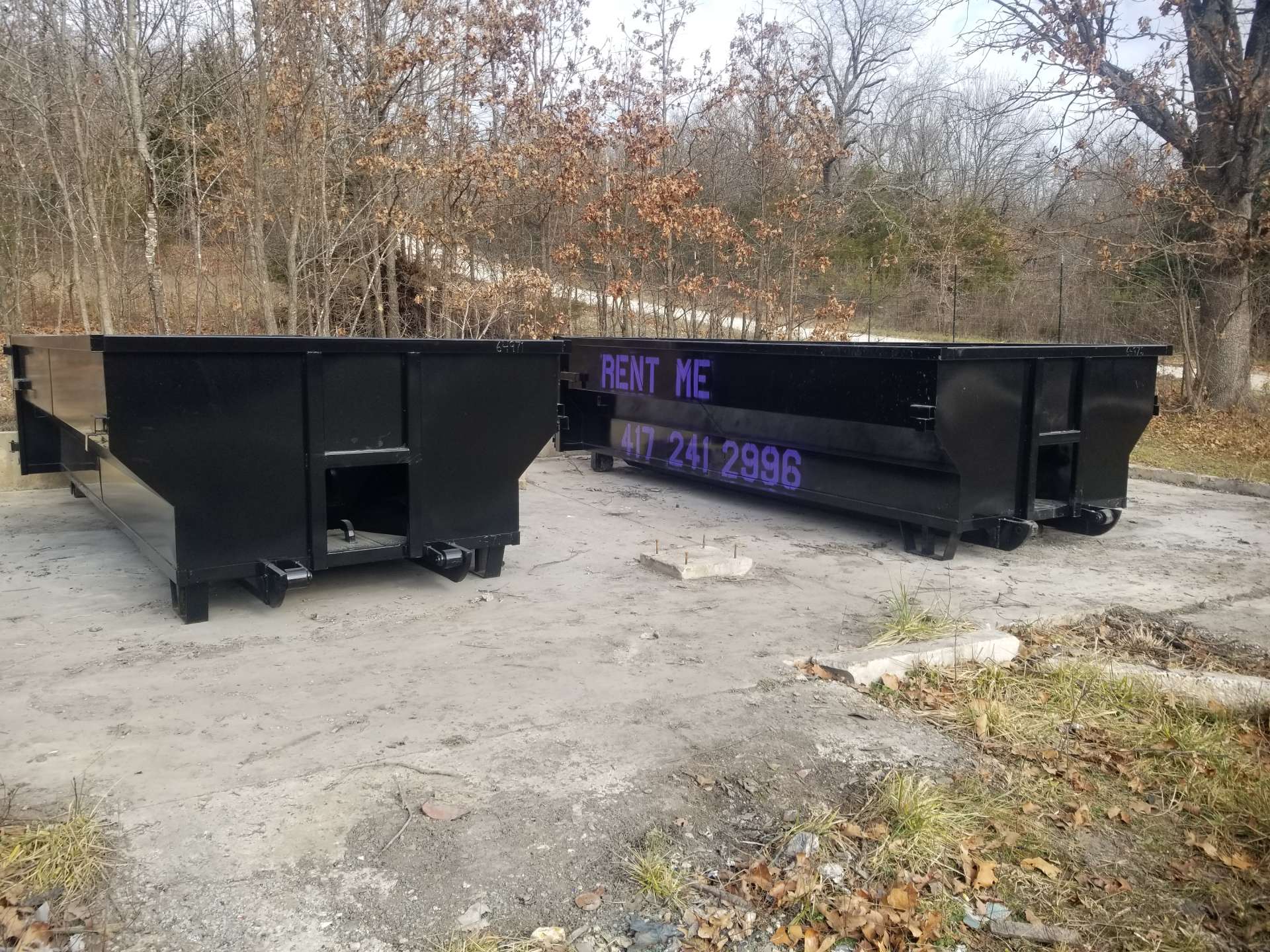 a black dumpsters on a dirt surface