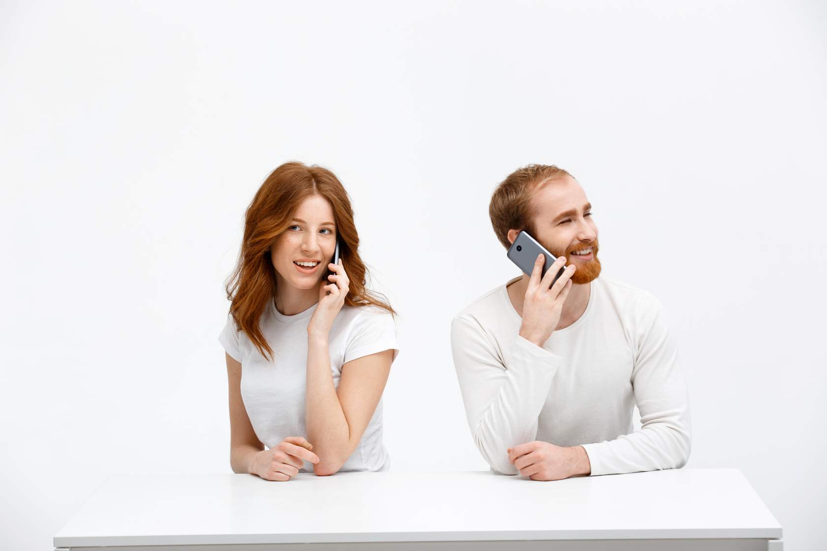 a man and woman sitting at a table talking on phones