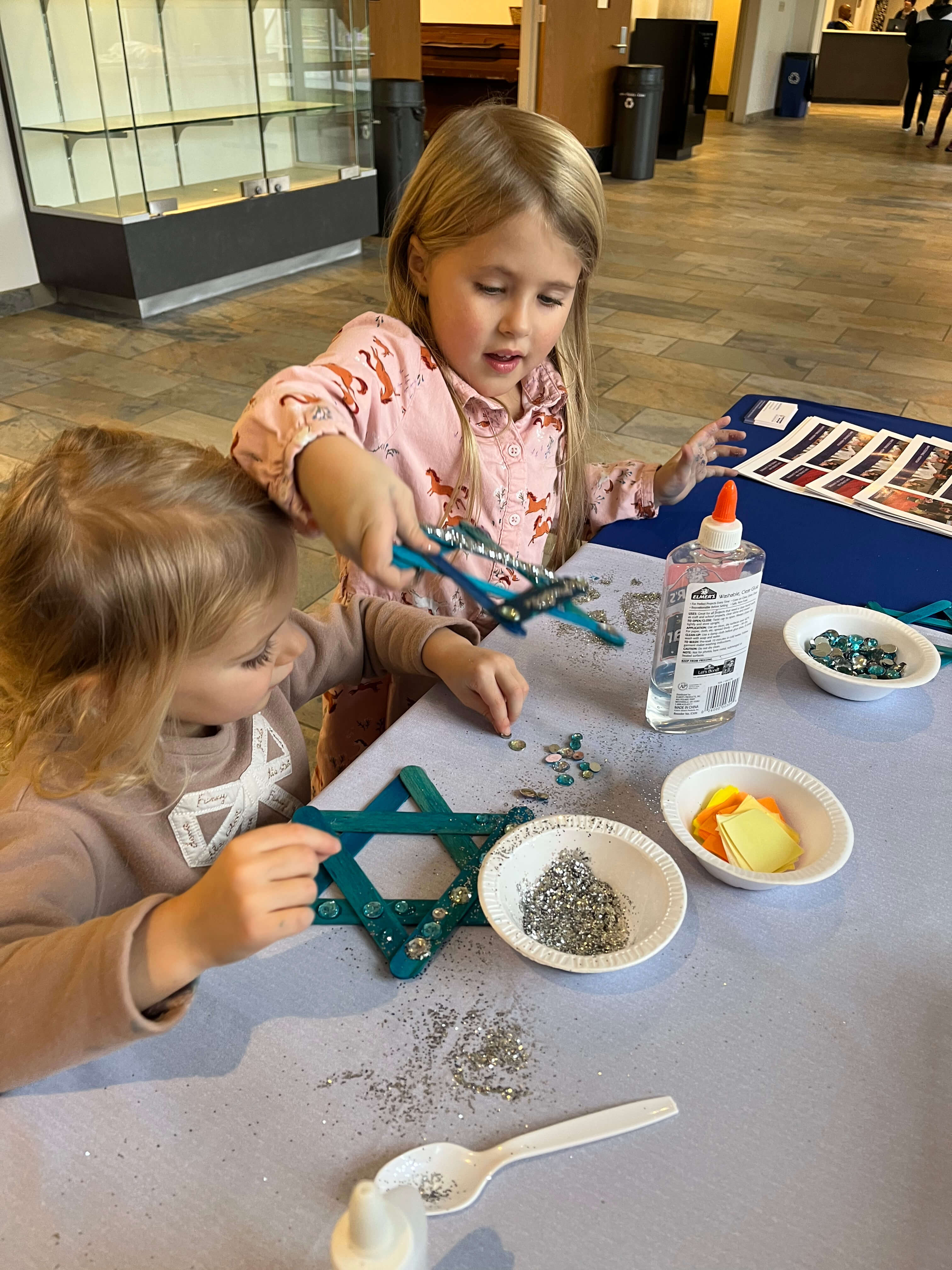two girls sitting at a table making glitter