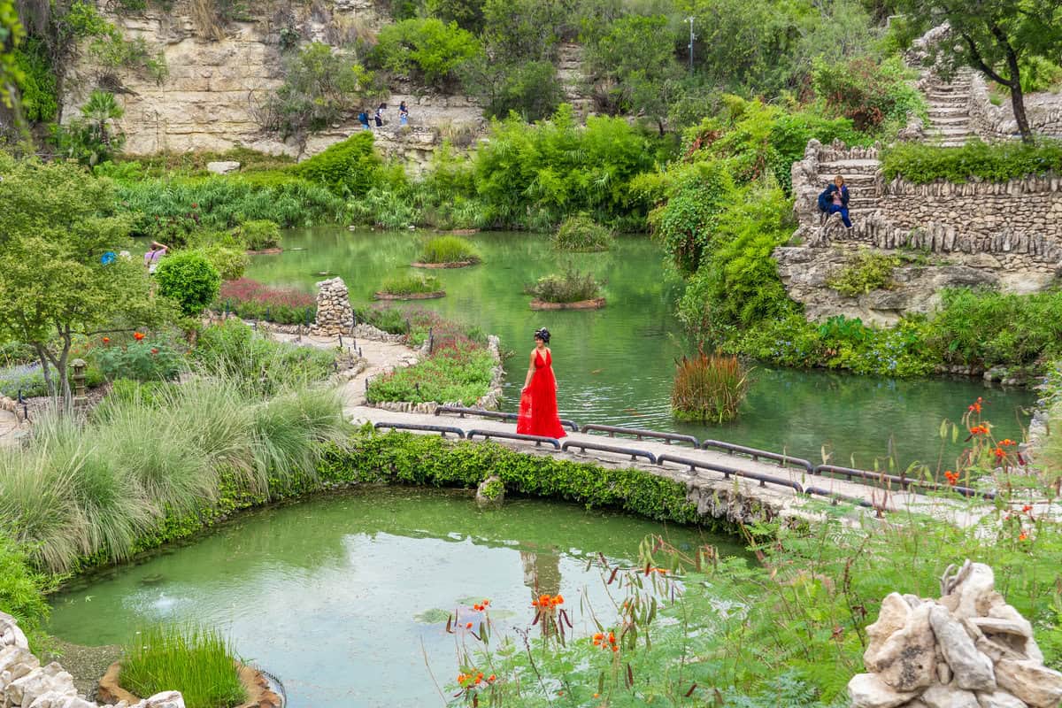 a woman in a red dress standing on a bridge over a pond