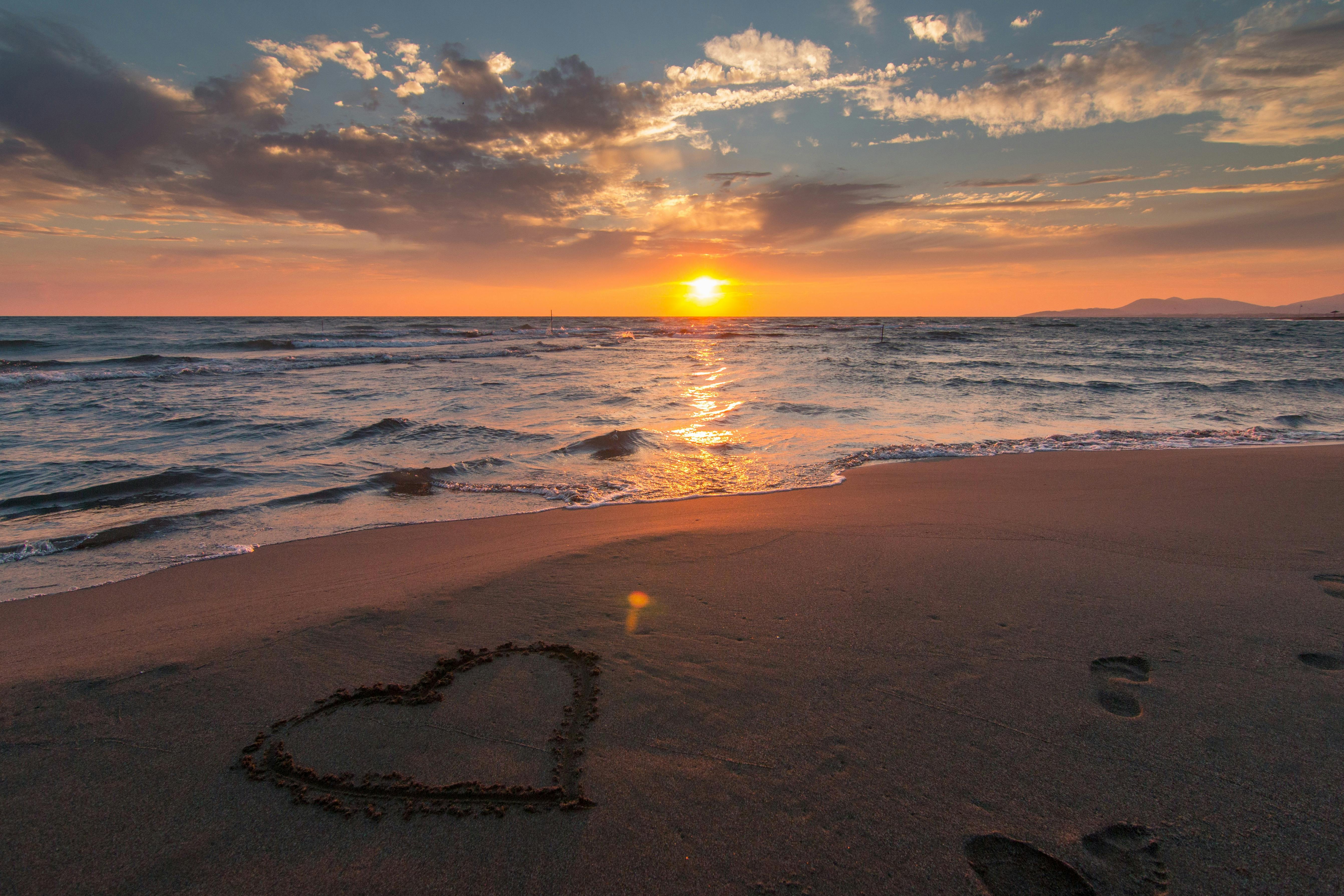 a heart drawn in sand on a beach with the sun setting in the background