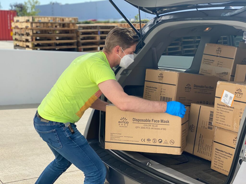 a man wearing a mask and gloves loading boxes into a car