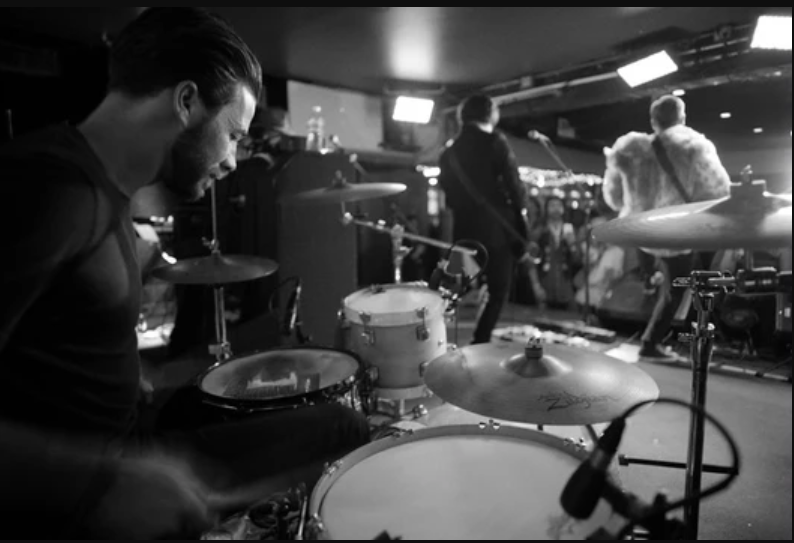 a man playing drums in a room with people in the background