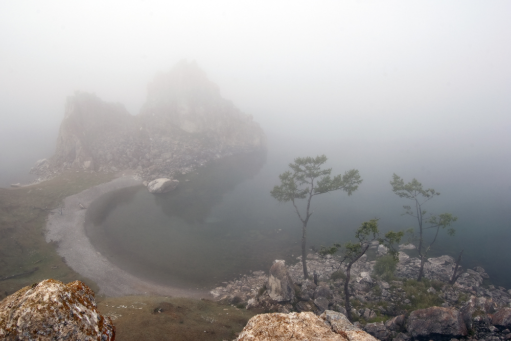 a foggy landscape with rocks and a lake