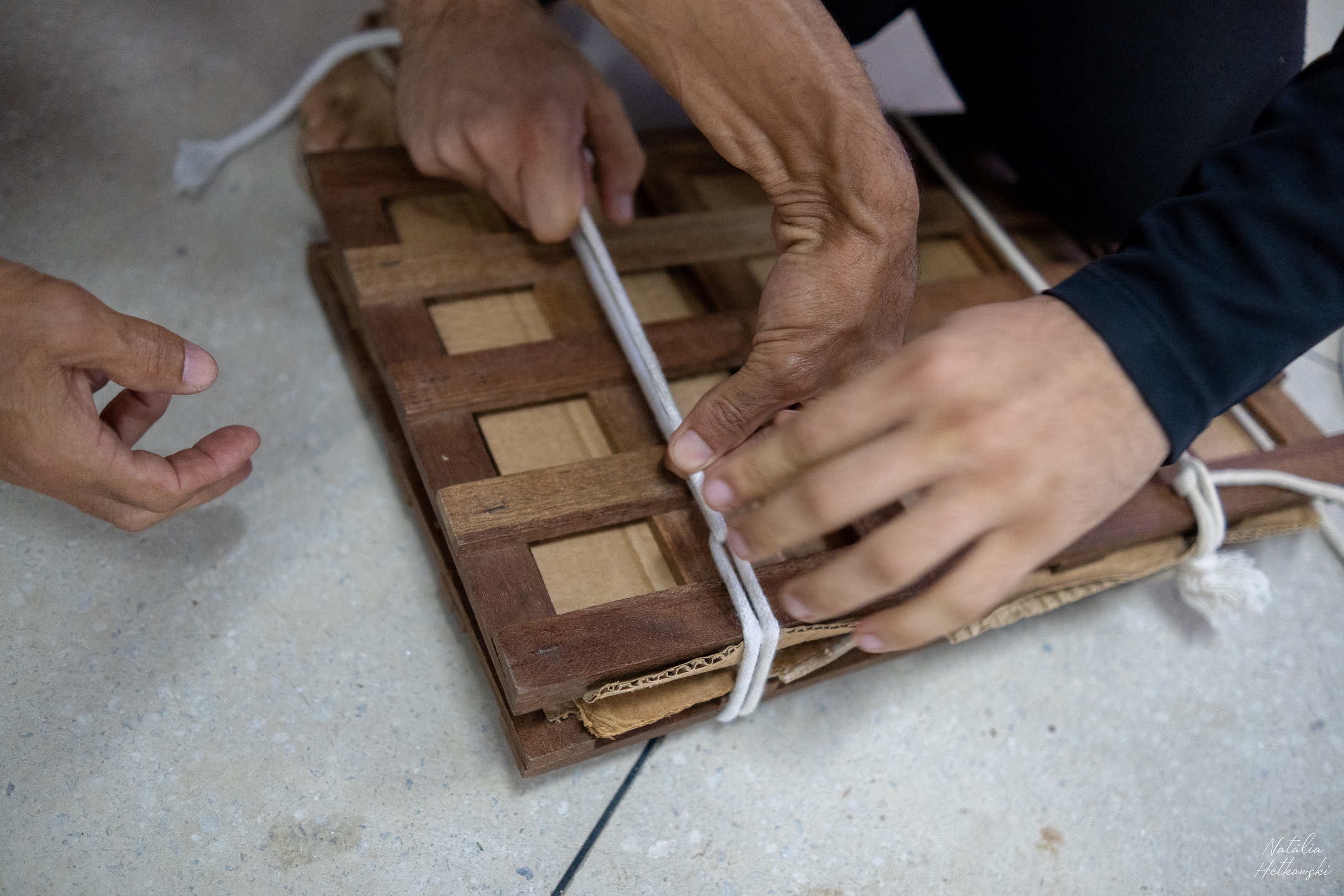 hands tying a string on a wooden piece of wood