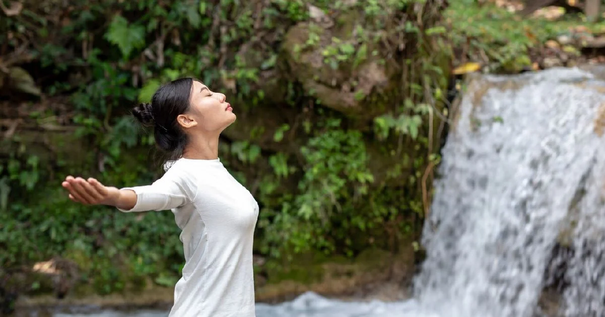 a woman with her eyes closed and arms outstretched in front of a waterfall