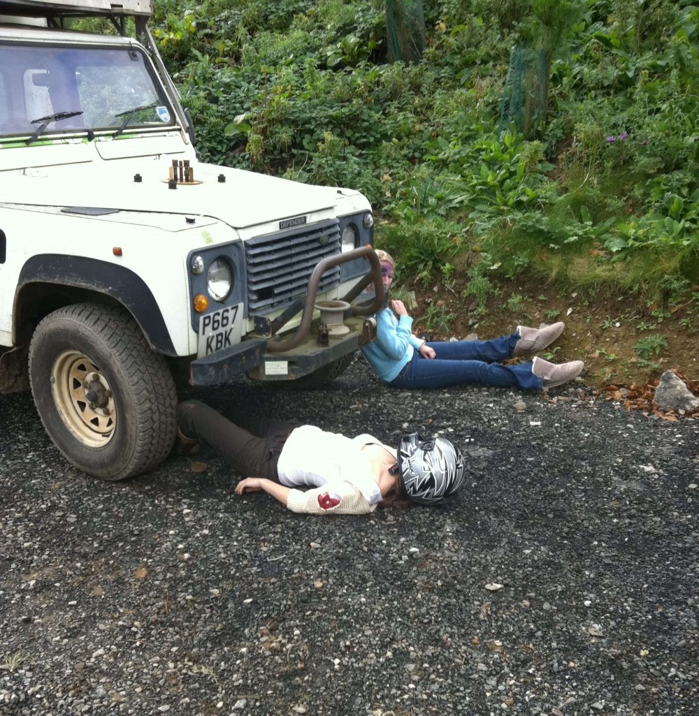 two people lying on the ground under a car