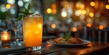 a glass of orange liquid with a leaf on top of a plate of food