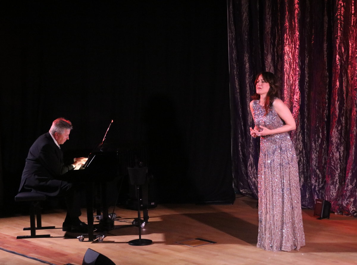 a woman in a dress on a stage with a man playing a piano
