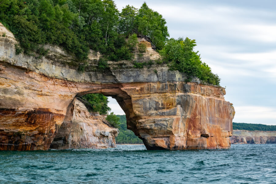 a rock cliff with trees on the side with Pictured Rocks National Lakeshore in the background