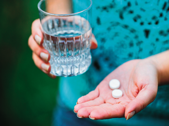 a hand holding a glass of water and two pills