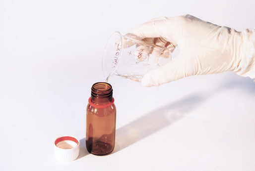 a hand pouring liquid into a small brown bottle