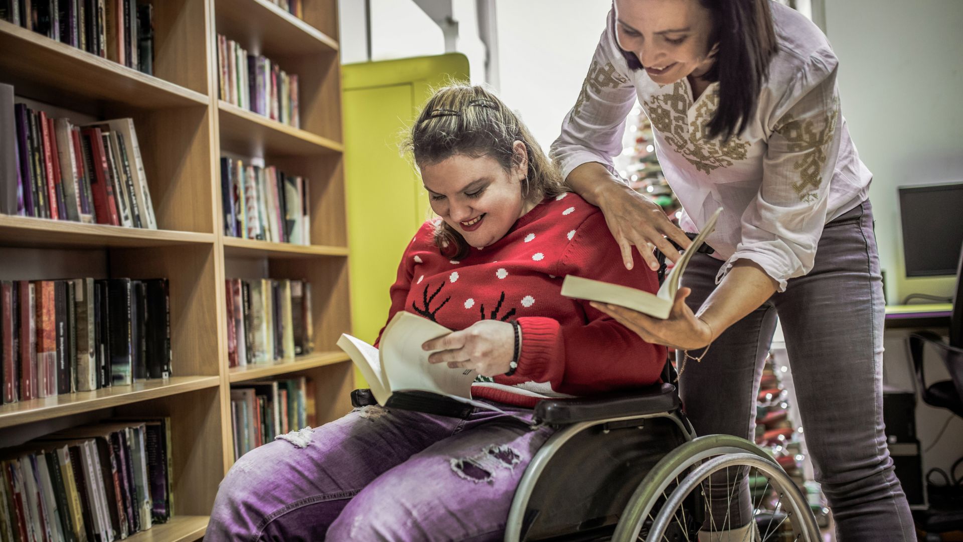 a woman helping a woman in a wheelchair reading a book