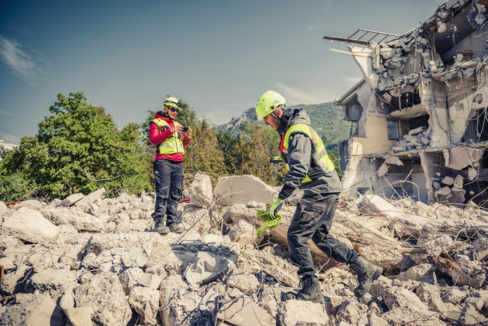 a man and woman in safety vests and helmets standing in rubble