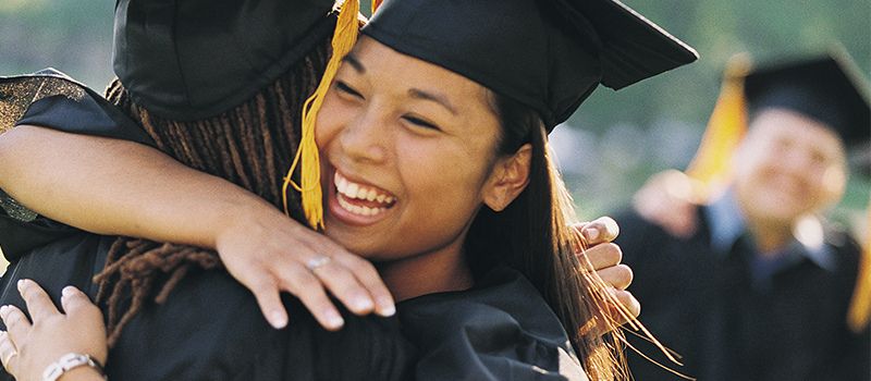 a woman in a graduation cap and gown hugging another woman