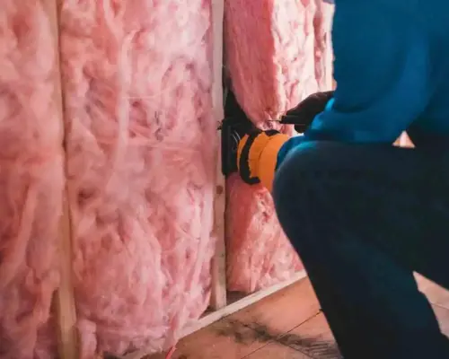 a person in a blue jacket and yellow gloves working on a wall with pink insulation