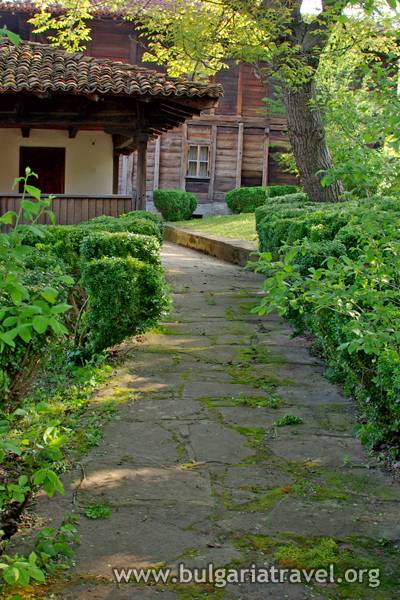 a stone path with bushes and a building in the background