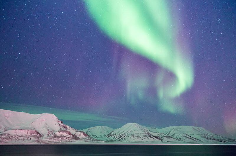 a green and purple aurora borealis over snowy mountains