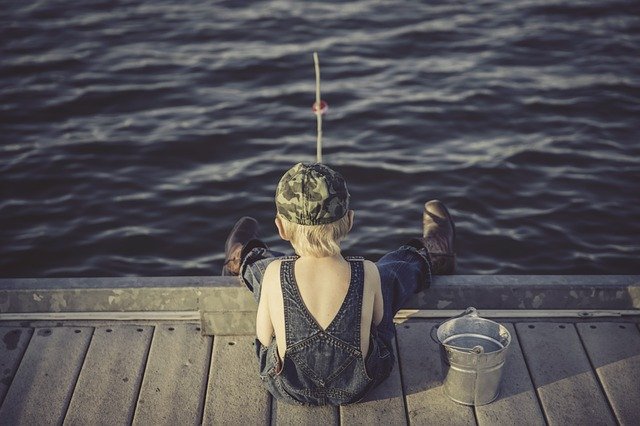 a boy sitting on a dock looking at the water