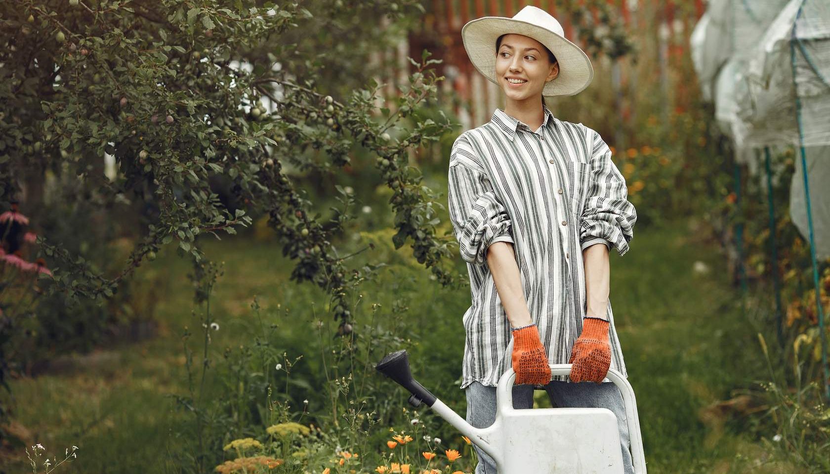 a woman wearing a hat and gloves holding a watering can
