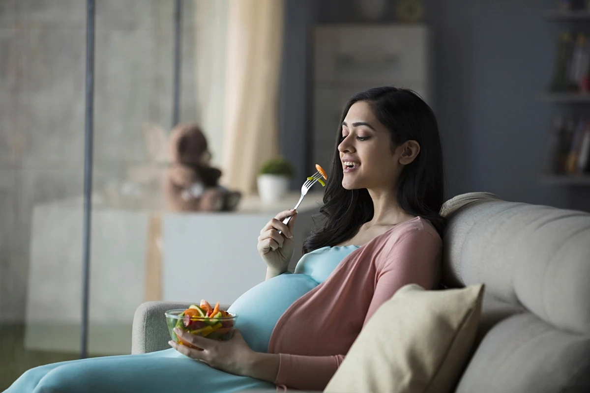 a pregnant woman sitting on a couch eating a salad