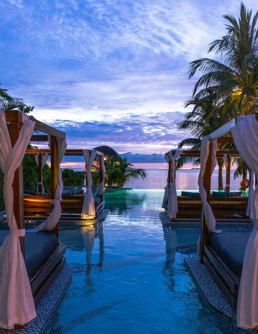 a pool with beds and palm trees and a sunset