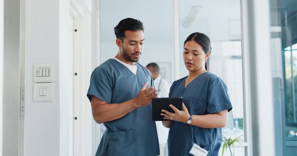 a man and woman wearing scrubs looking at a tablet