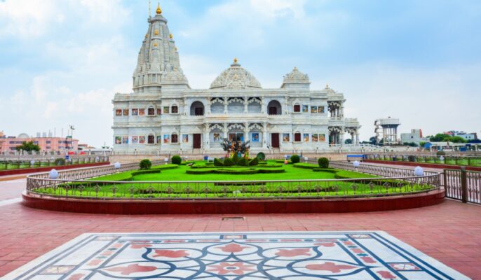a white building with a garden and a tiled floor with Prem Mandir Vrindavan in the background