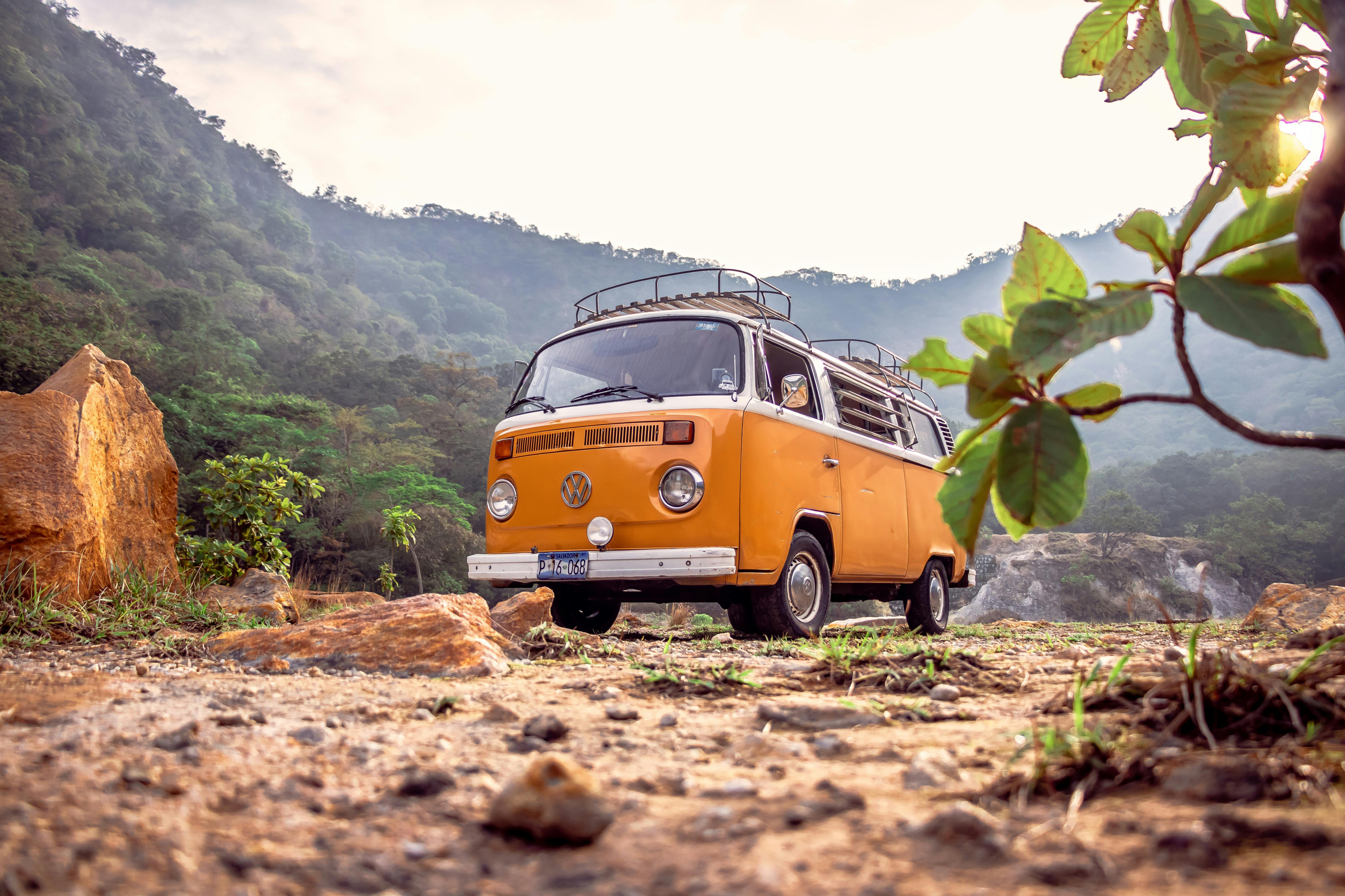 an orange van parked on a dirt road with trees and mountains in the background
