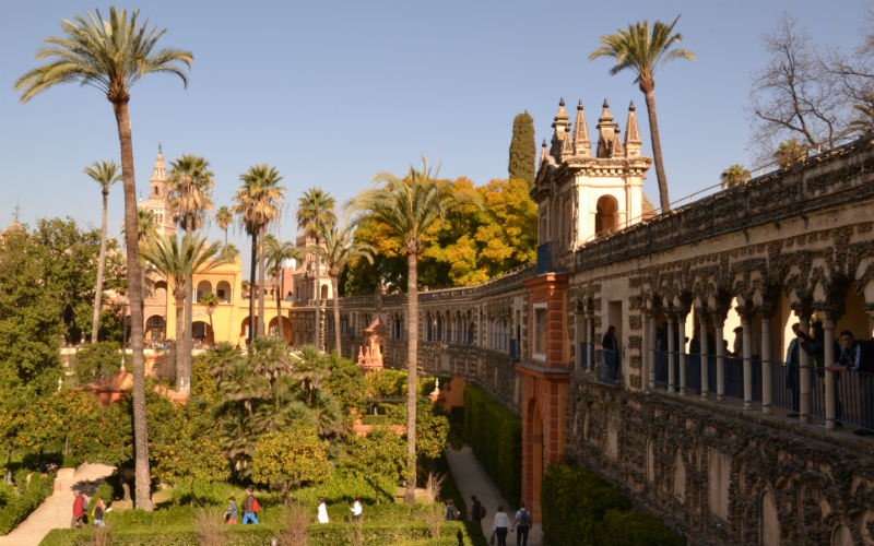 a courtyard with many trees and Alcázar of Seville with a stone wall