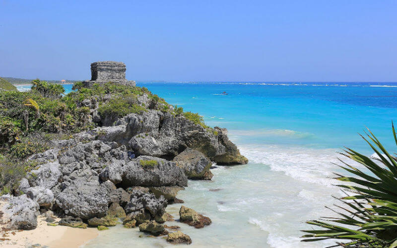 a rock structure on a rocky beach with Tulum in the background