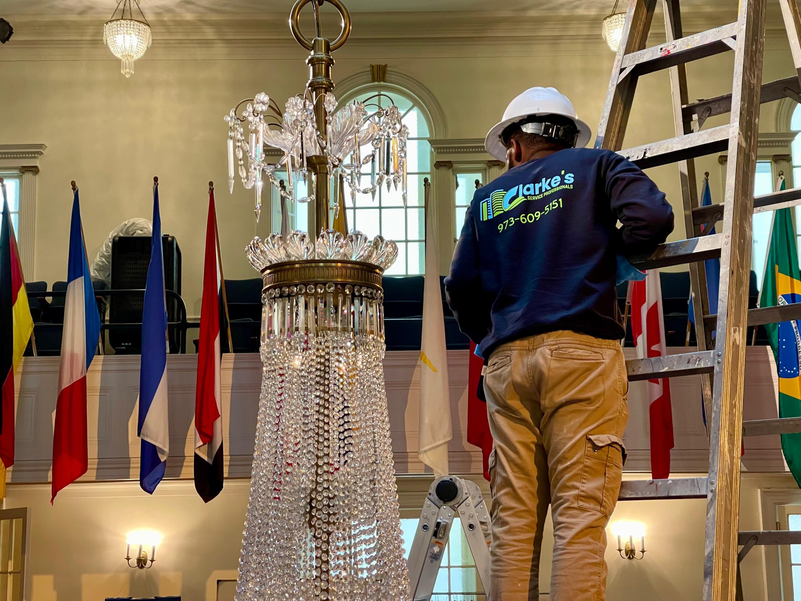 a man standing on a ladder next to a chandelier