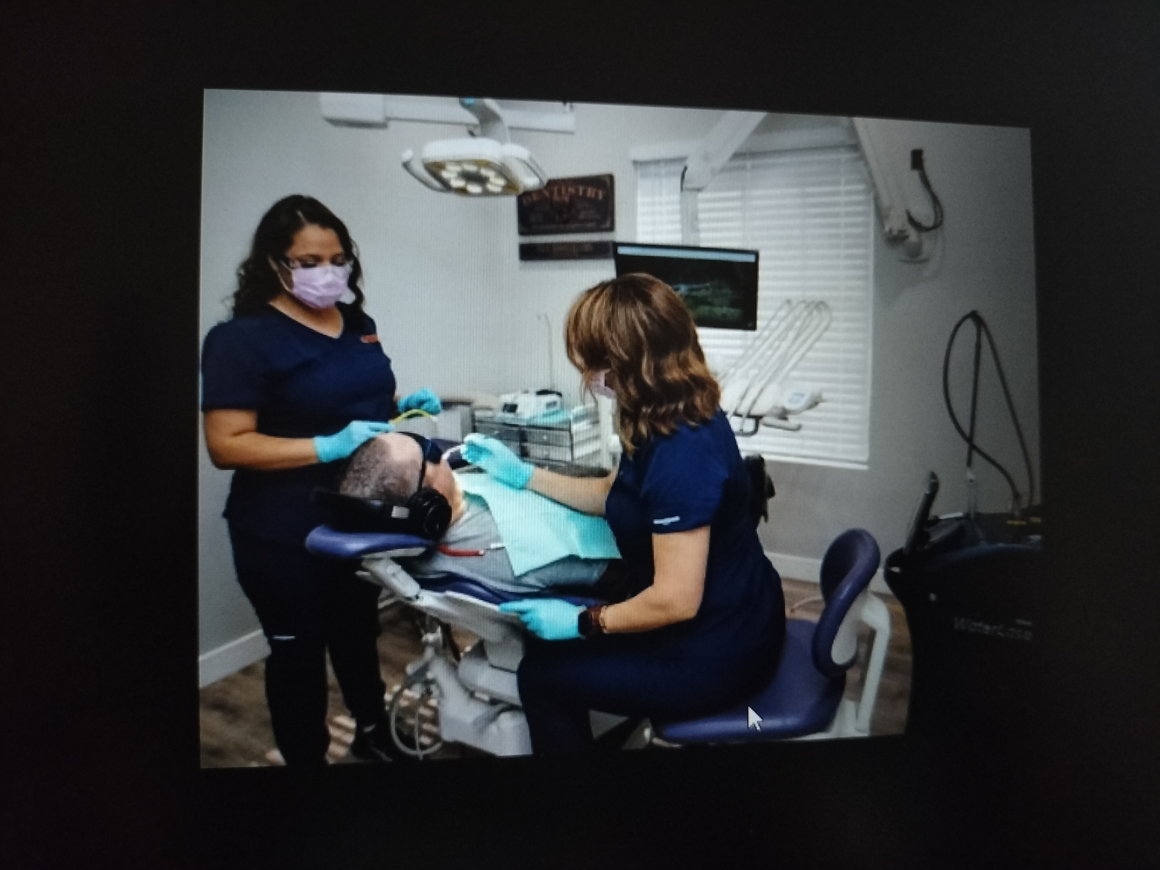 a woman in blue scrubs and gloves working on a patient