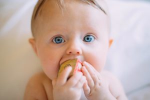 a baby with blue eyes biting a block