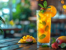 a glass of orange juice with mint leaves and fruit on a table