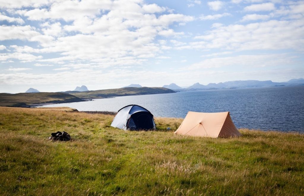 tents on a grassy hill next to a body of water