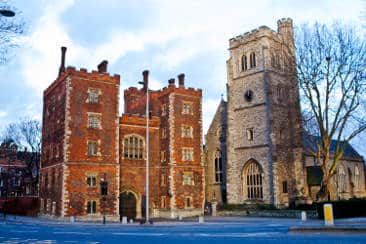 a brick building with a clock tower with Lambeth Palace in the background
