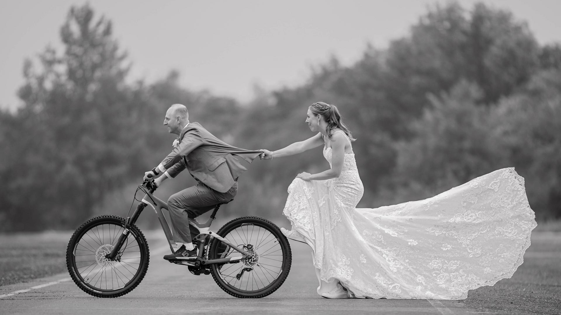 a man in a suit and a woman in a wedding dress riding a bicycle
