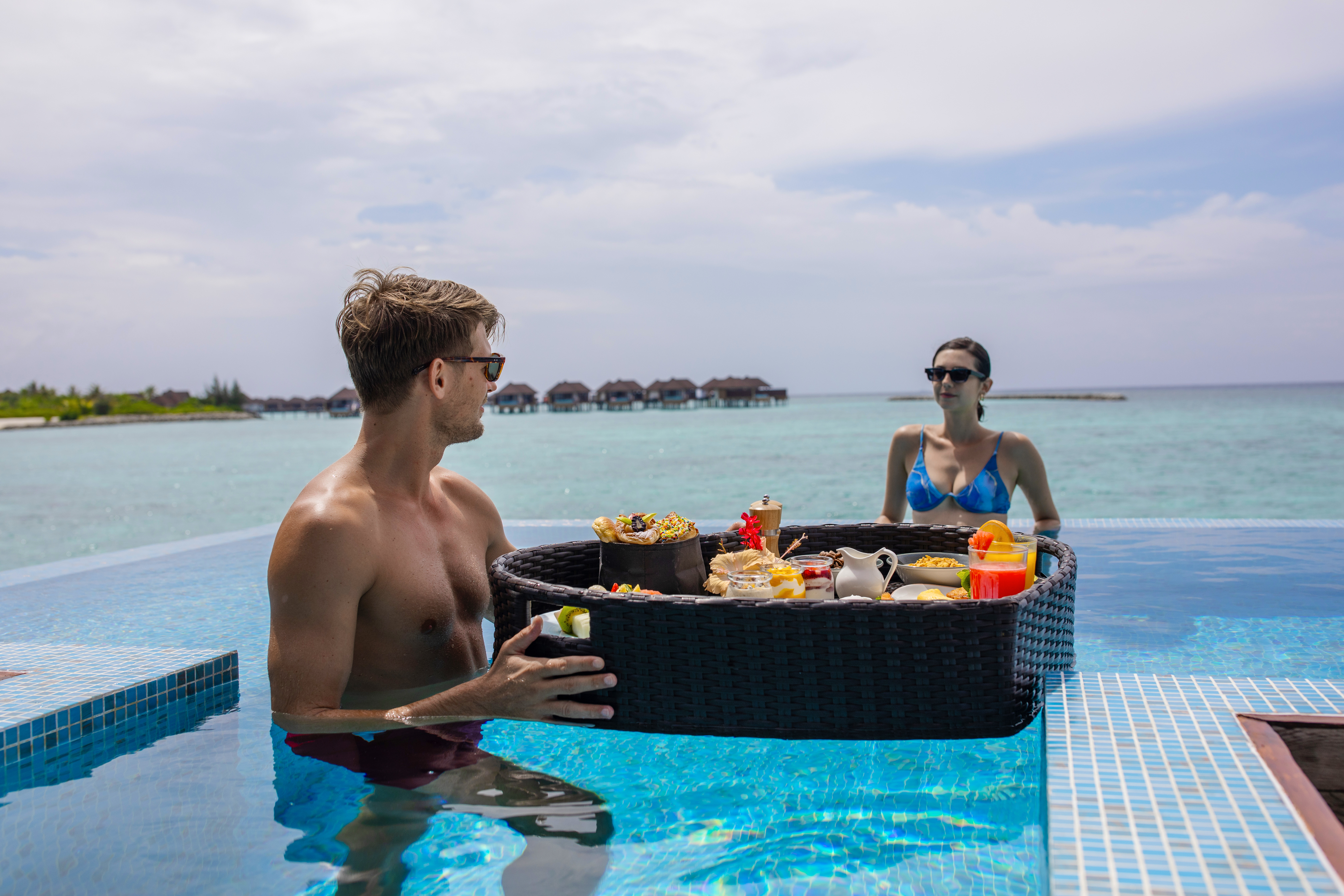 a man and woman in a pool with a tray of food