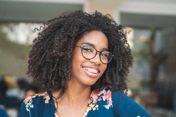 a woman with curly hair wearing glasses and braces smiling