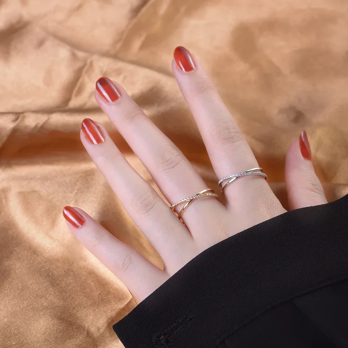 a hand with red painted nails and rings on a gold fabric