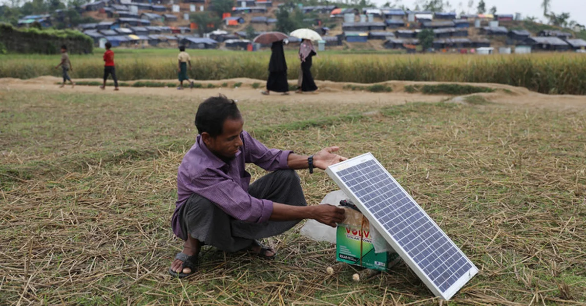 a man kneeling on grass with a solar panel