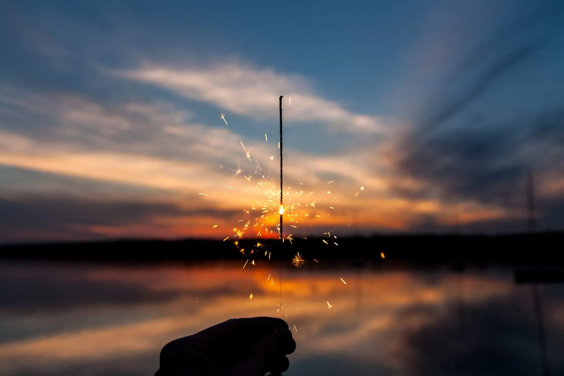 a hand holding a sparkler in front of a sunset